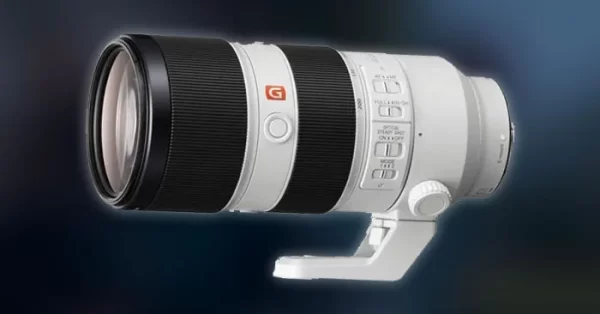 Fotógrafo usando câmera Sony Alpha com lente teleobjetiva branca em estádio de futebol durante o pôr do sol.