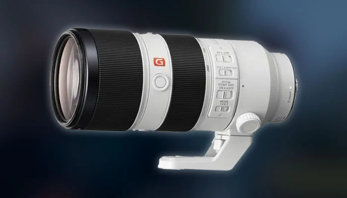 Fotógrafo usando câmera Sony Alpha com lente teleobjetiva branca em estádio de futebol durante o pôr do sol.