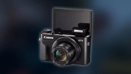 Câmera compacta Canon G7x com a tela virada para frente em cima de uma mesa de madeira