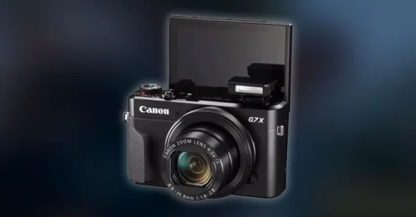 Câmera compacta Canon G7x com a tela virada para frente em cima de uma mesa de madeira